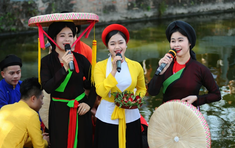 three asian women holding microphones in front of water