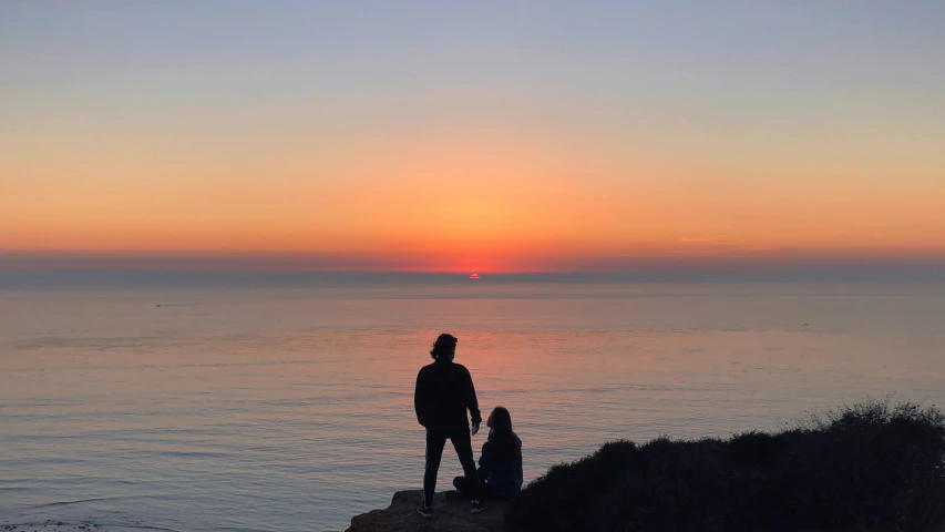 a couple watching the sun go down on the ocean