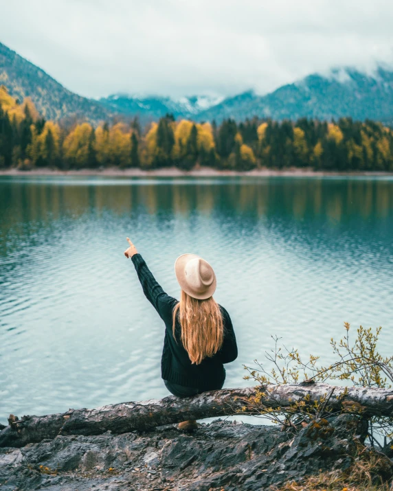 the girl is sitting on the rock by the water