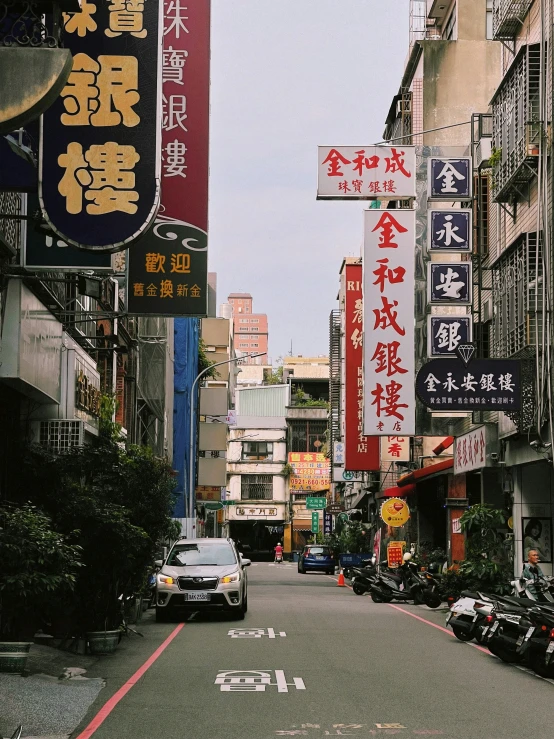 cars drive down a narrow chinese street with signage