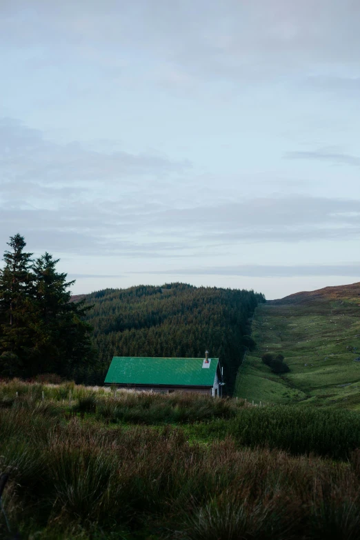 a lone white house nestled in the middle of green mountains