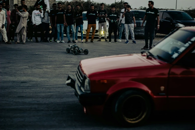 a group of people stand around a car and some people are watching