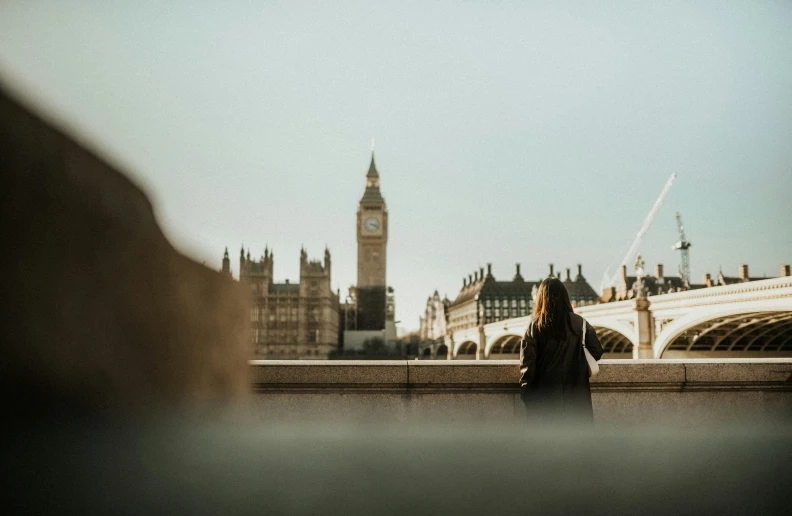 a lady is standing next to a bridge near the clock tower