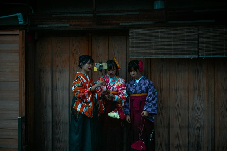 three young ladies stand beside a wooden wall