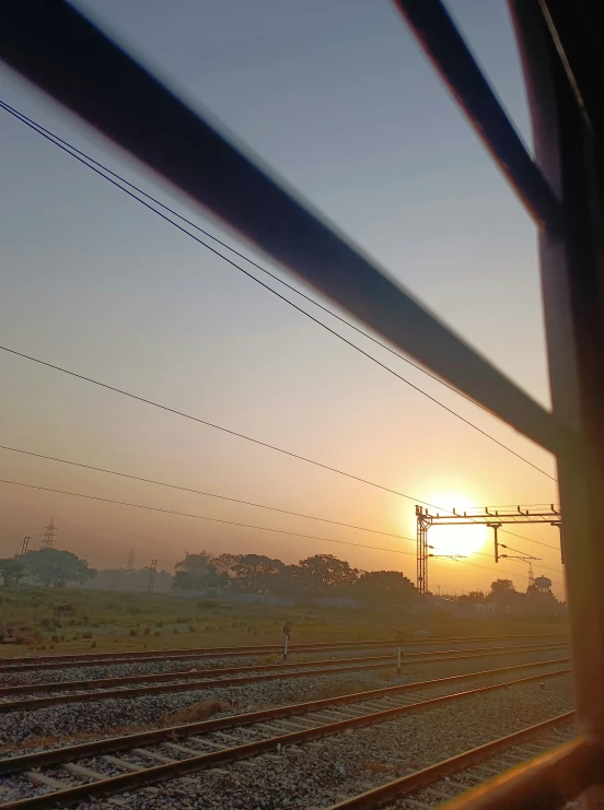 the sun setting behind an electrical fence on train tracks