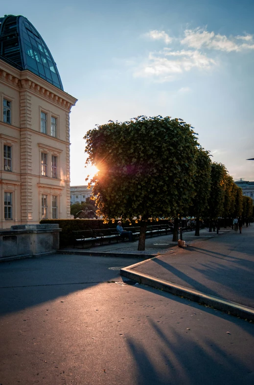 the sun is going down near a tree and building