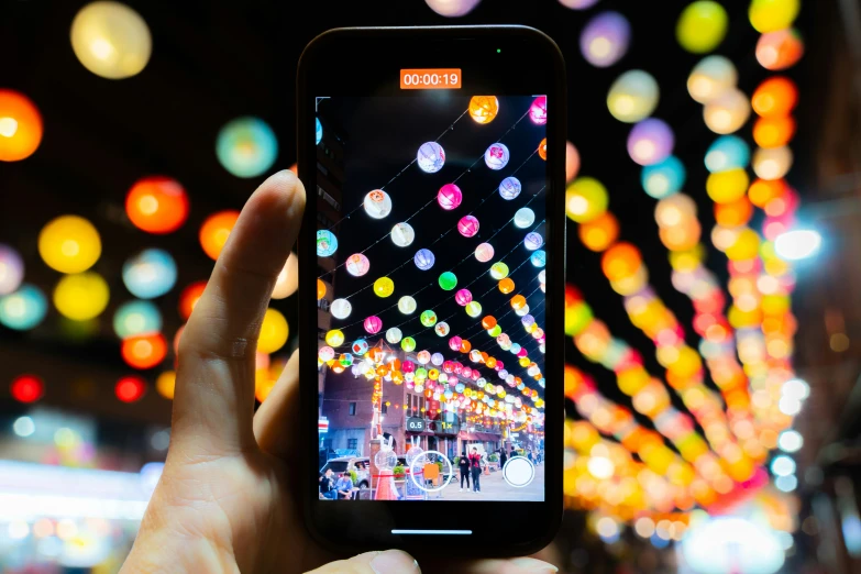 a person holding a phone with a lighted street scene in the background