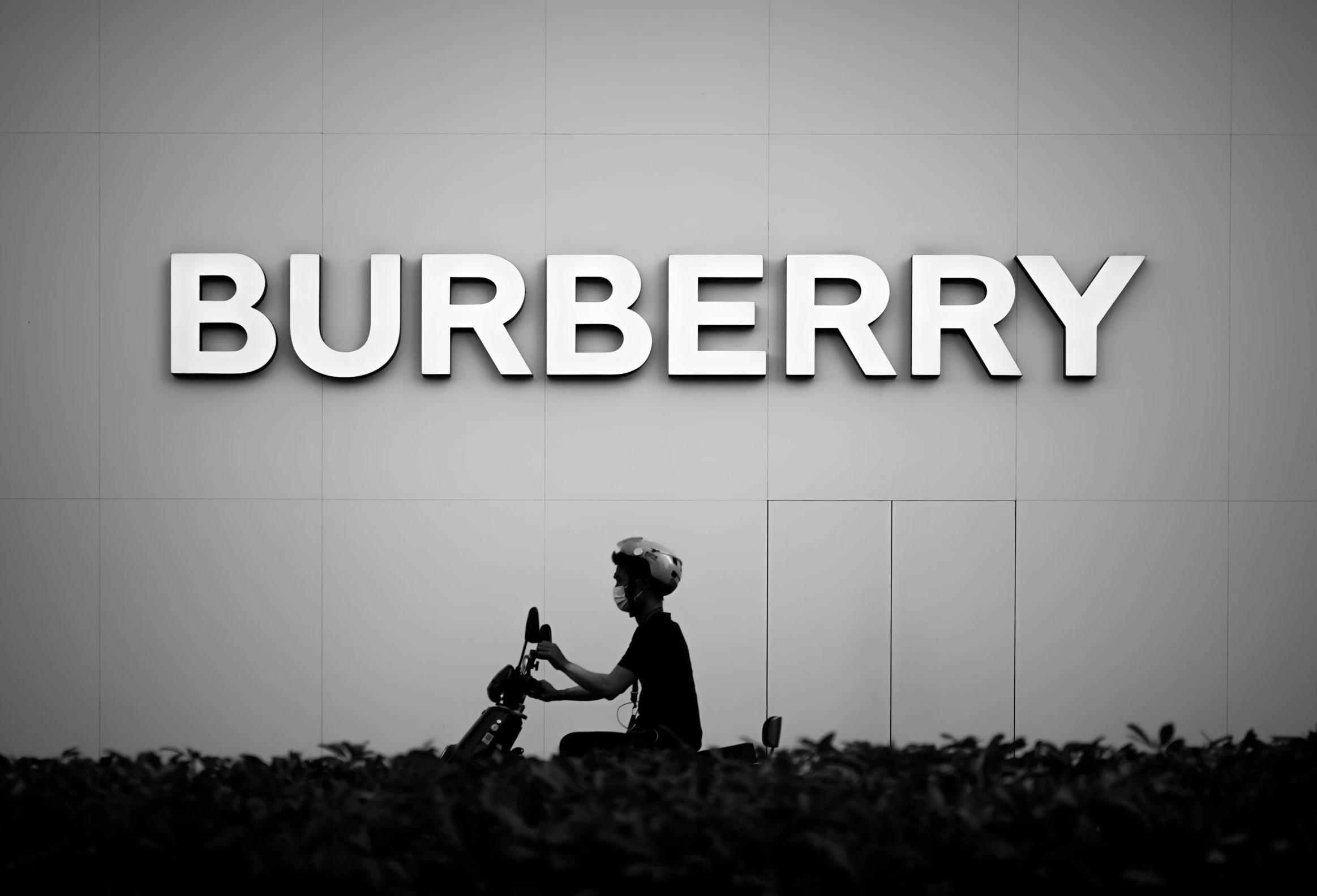 a man rides his motorcycle past the sign for burbery