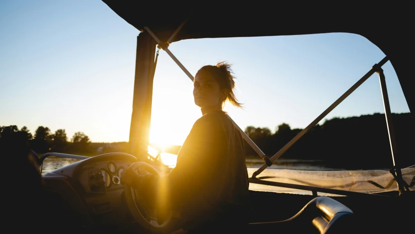 a woman sitting on top of a boat at sunset