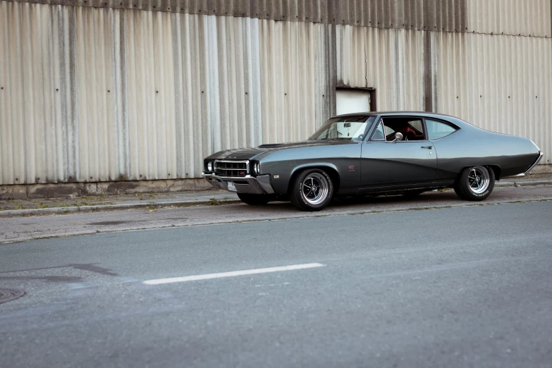 a black car sitting on the side of a road next to a tall wall