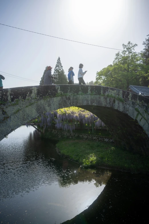 three people on a bridge over a pond