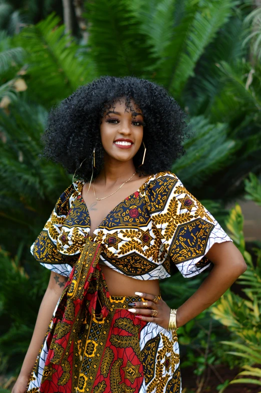 a woman in a top and skirt stands in front of bushes