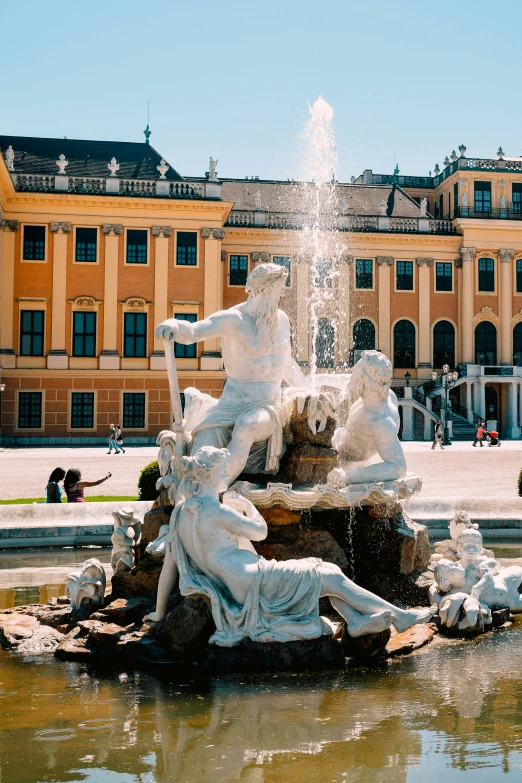 a fountain in front of a large building with some people sitting