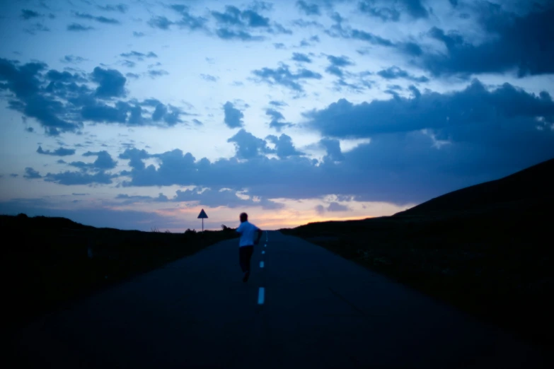 a man walking along a path during sunset with his skateboard