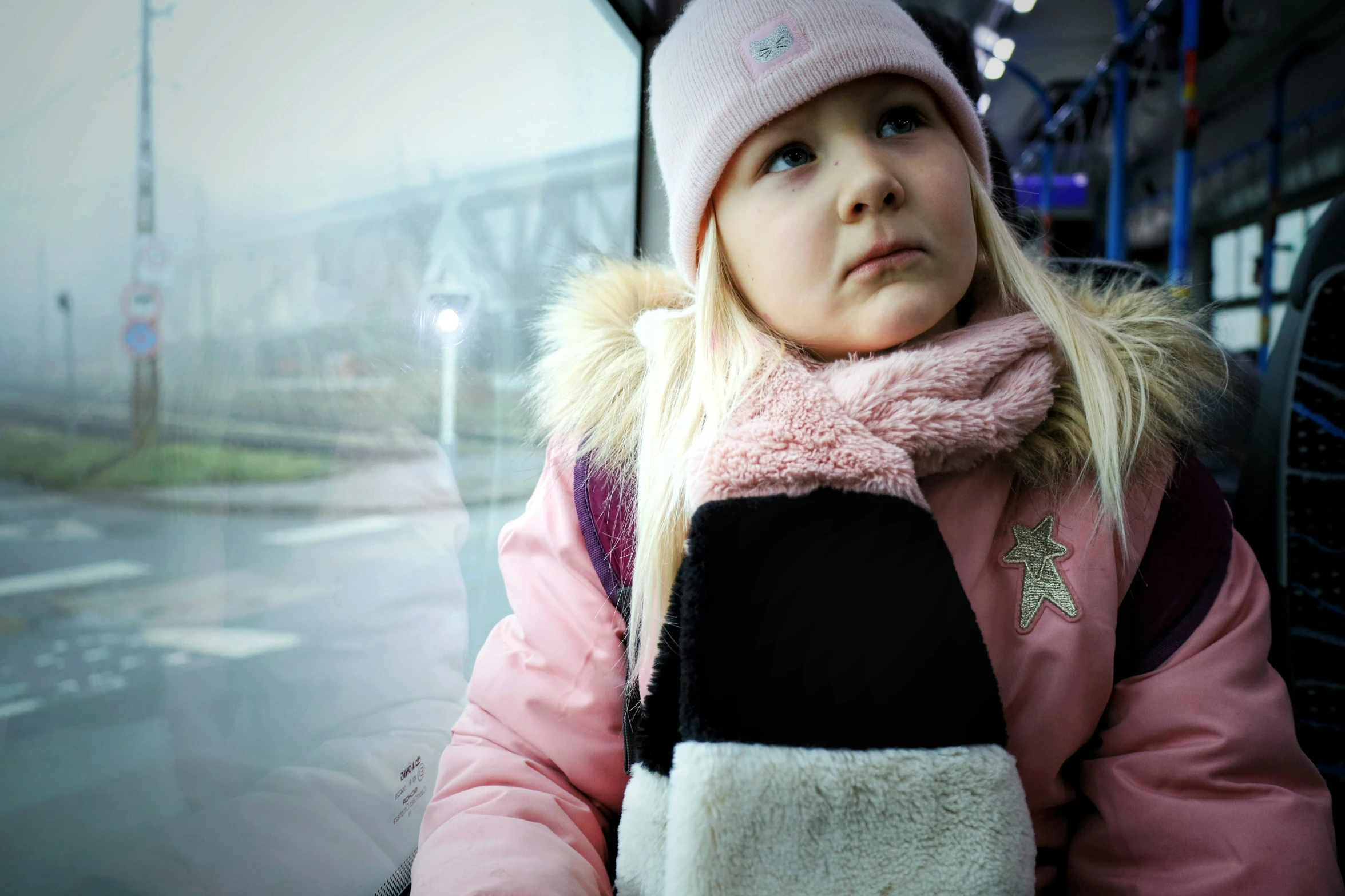 little girl in pink coat and hat looking at the side of a bus