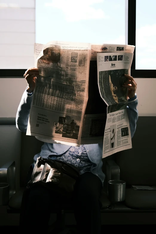 a person reads an open newspaper while riding a subway