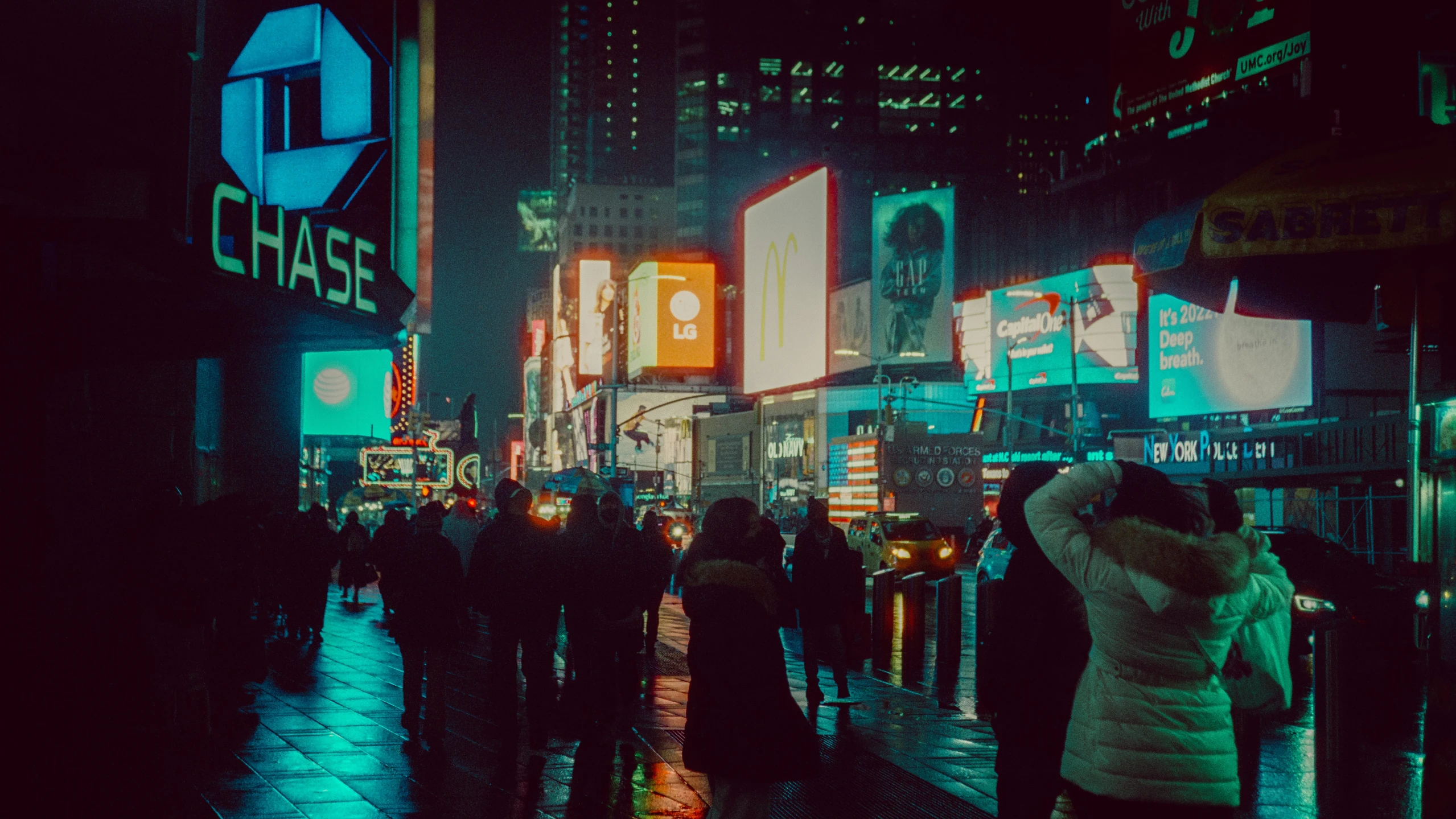 people walking in the city at night with city lights and signs on a building