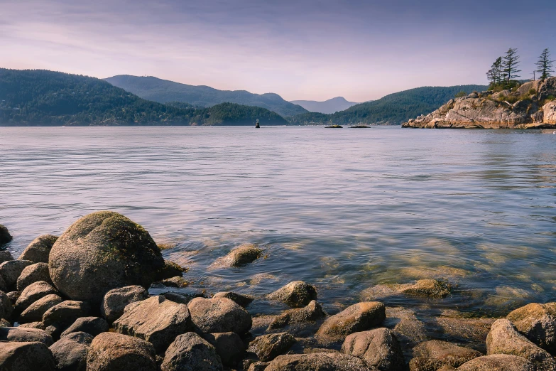 water with rocks near the shore and mountains in the background