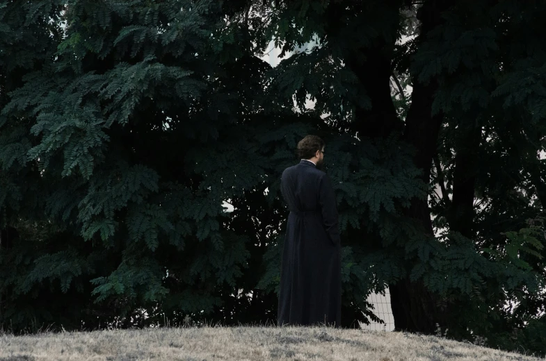 woman in black dress standing by some green trees