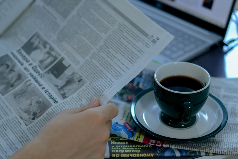 newspaper on table with coffee cup and human hand