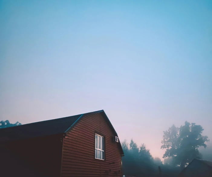 a brown building next to trees with a fogy sky