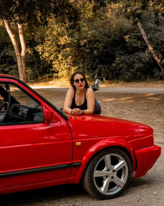 a girl is leaning against the door of a red car