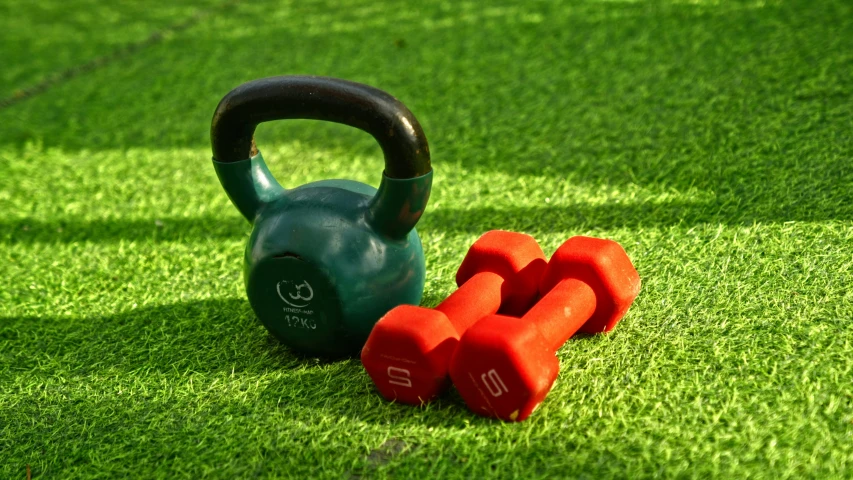 three colorful dumbbells and two green kettles in the grass