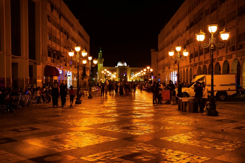 a nighttime city street scene with people standing and sitting
