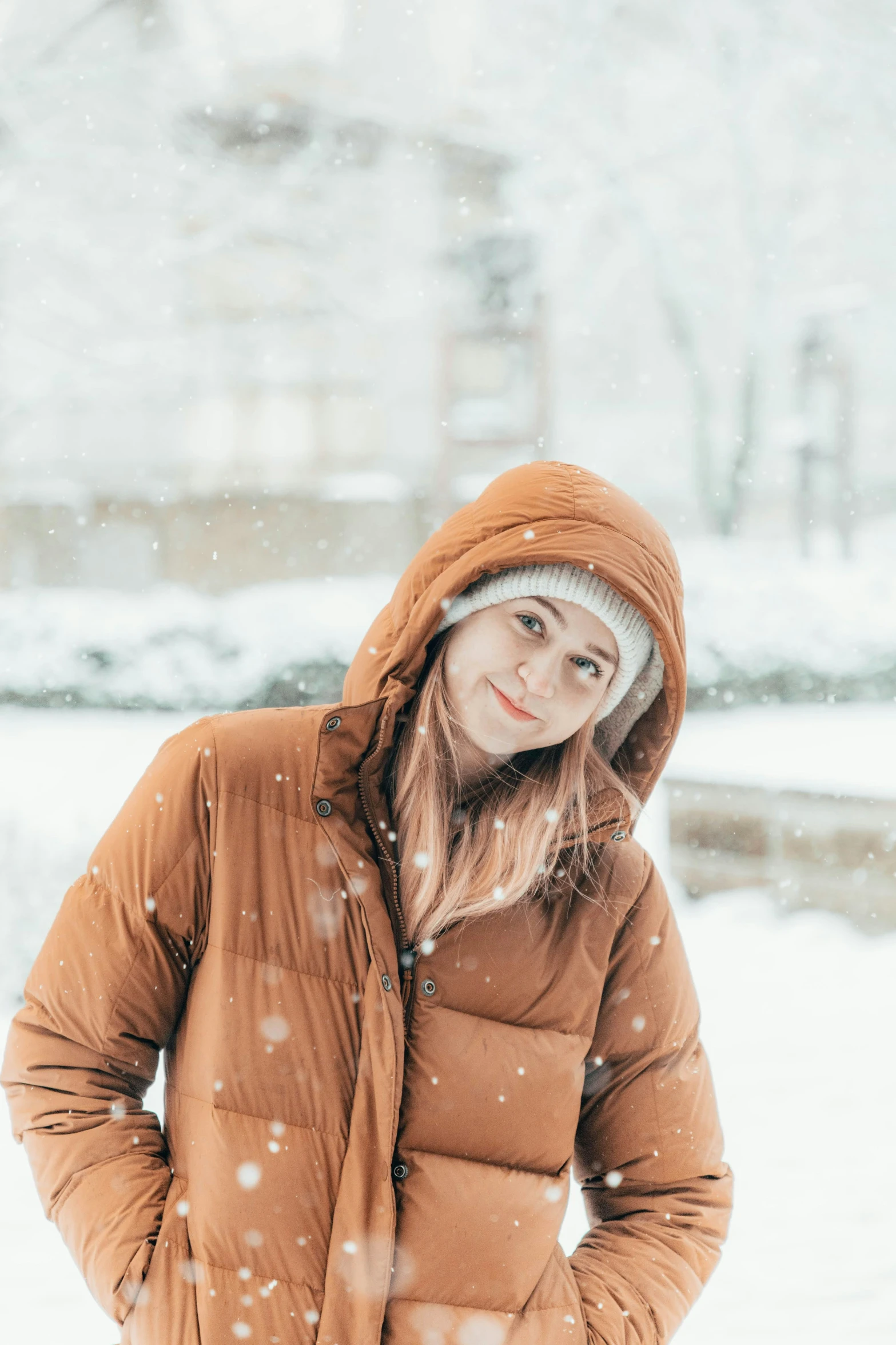 young woman standing in snow looking away from camera with hood up