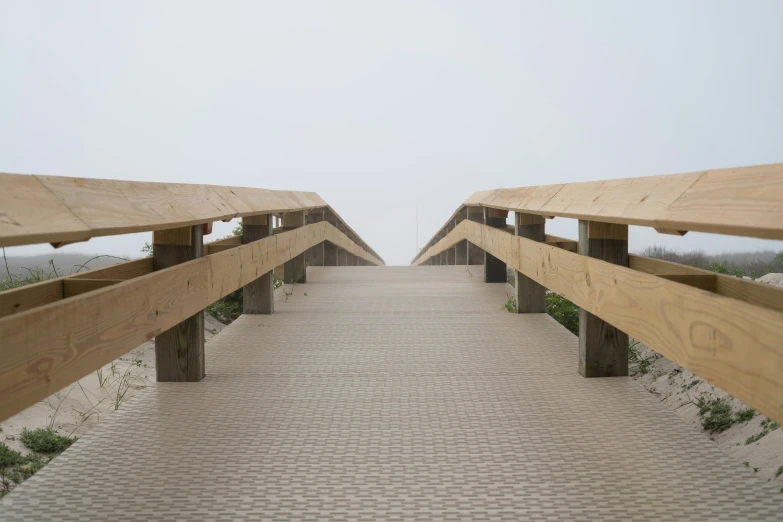 a wooden walkway leads to the beach on a foggy day