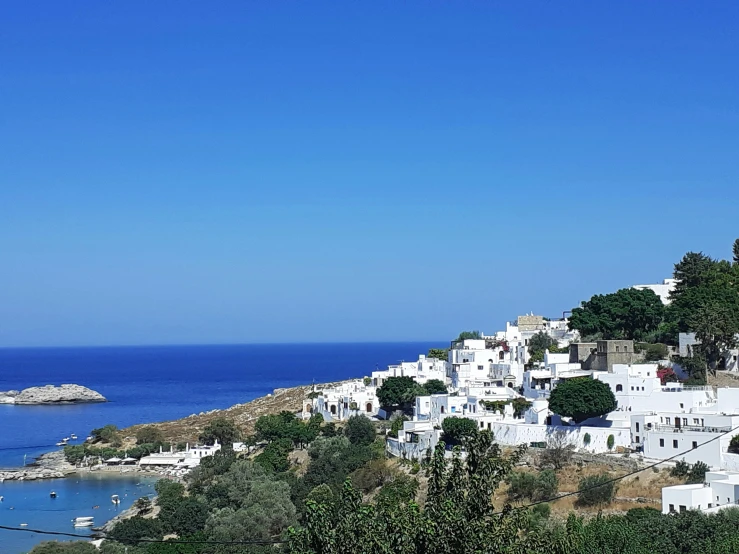 white houses are situated along a steep cliff with blue sea in the background