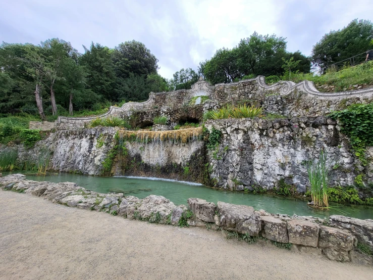 a waterfall with rocks and plants and a sandy beach