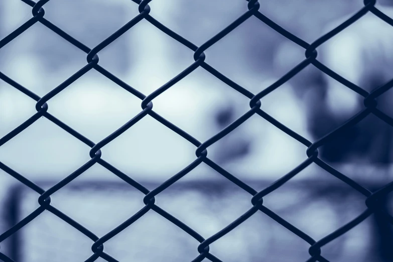 closeup view through a chain link fence with a person walking on the street behind it