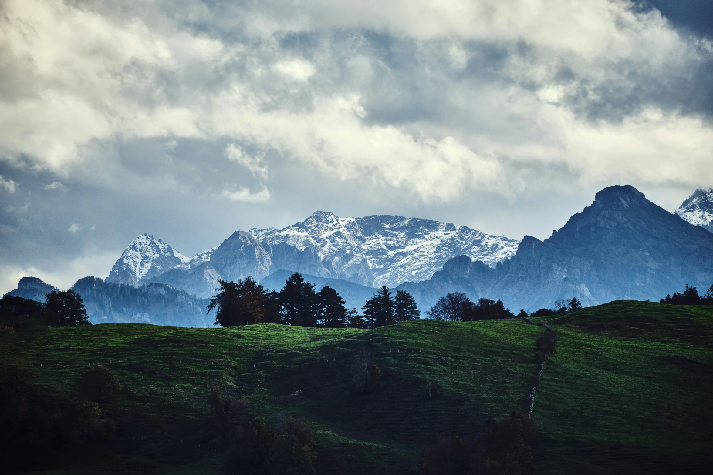 this is mountains with clouds and grass in the foreground