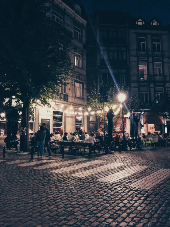 several people sitting at a table outside on cobblestone streets