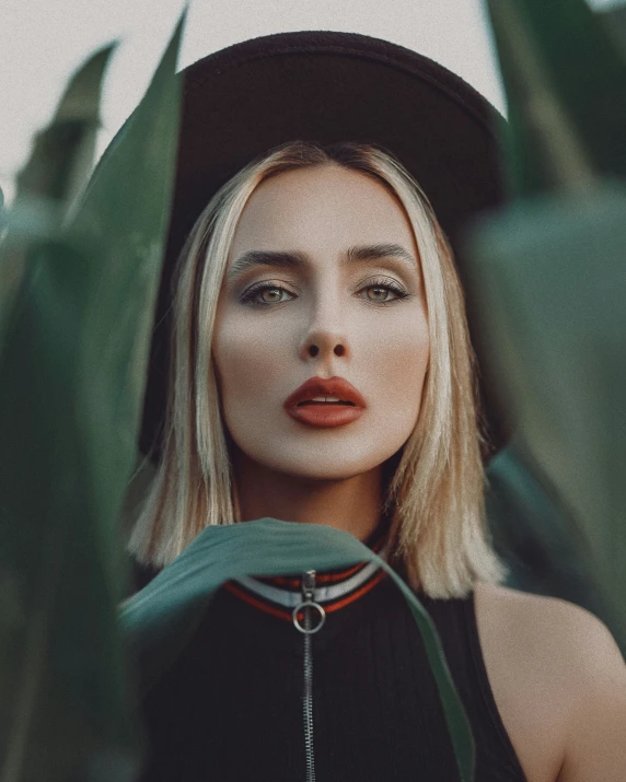 blonde haired woman with hat standing in green plant