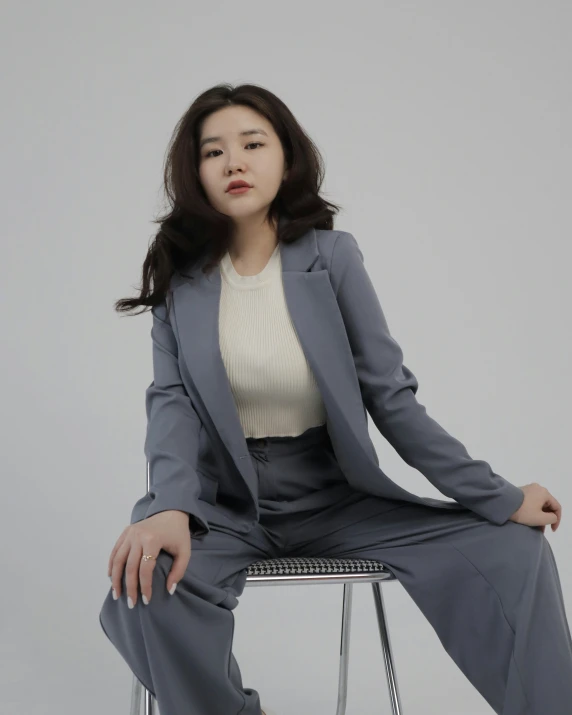 a woman in grey suit sitting on a stool