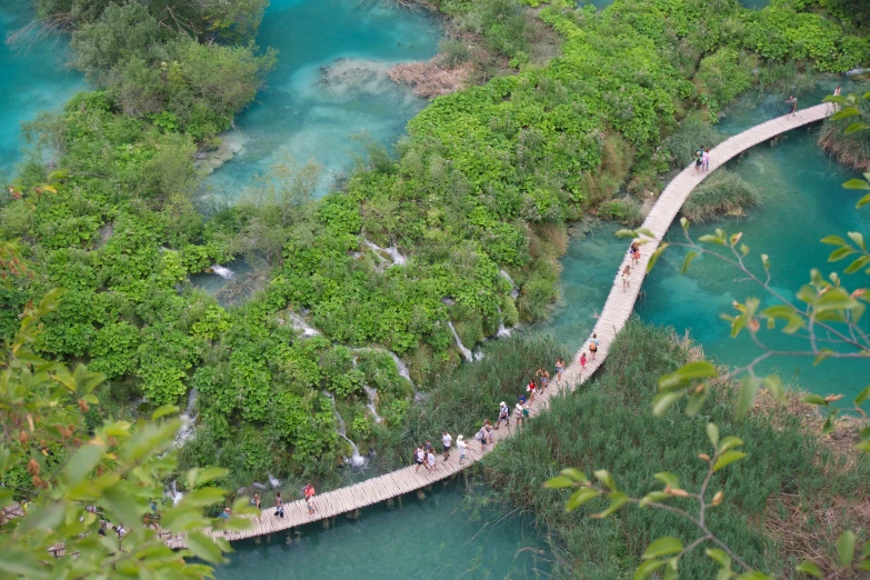 people walking over the blue waters on a wooden bridge