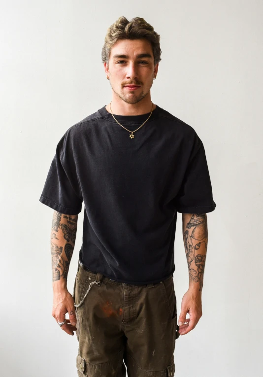 a man with tattoos stands in shorts and shirt