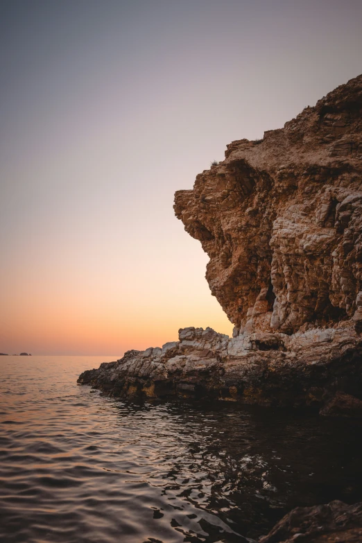 a person on rocks on the water near some cliffs