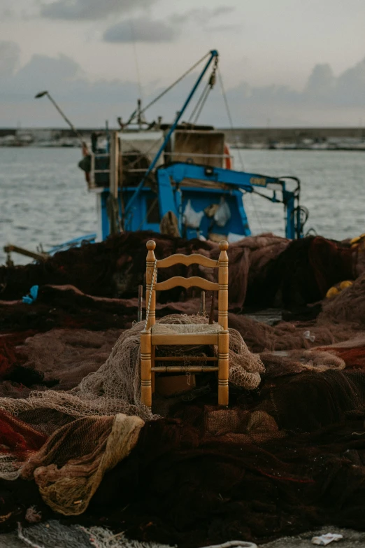 a wooden chair is on the rocks near a boat