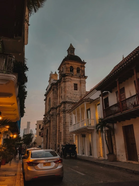 a street scene with cars parked and an old church in the background