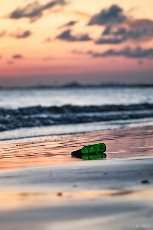 a green bottle laying on a sandy beach at dusk