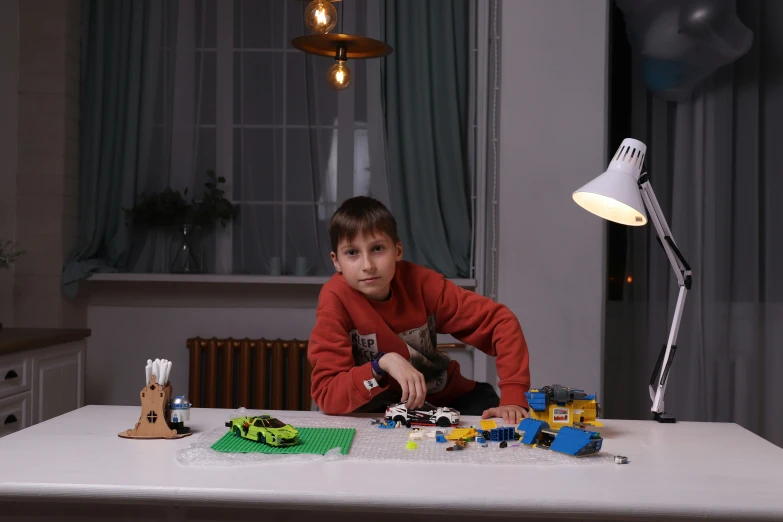 boy in red shirt sitting at table with small toy car