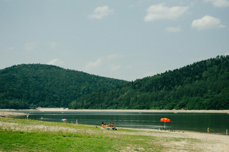 people sitting on a beach near a mountain lake