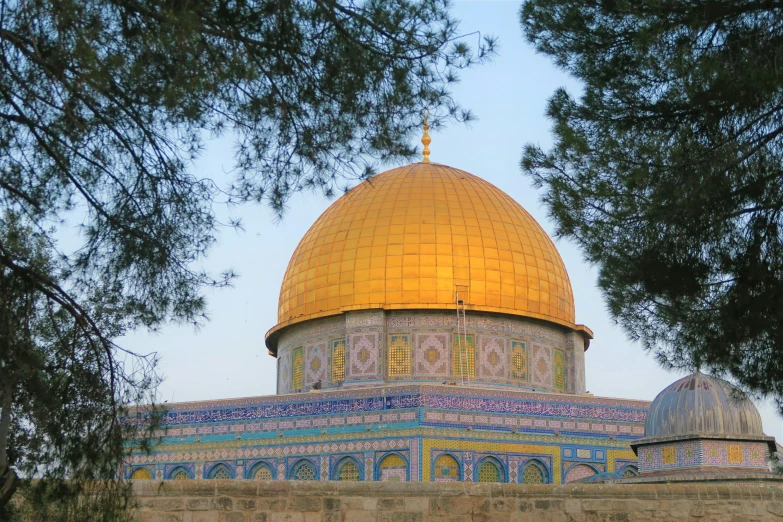 an ornate domed building with a golden dome and two columns under some trees