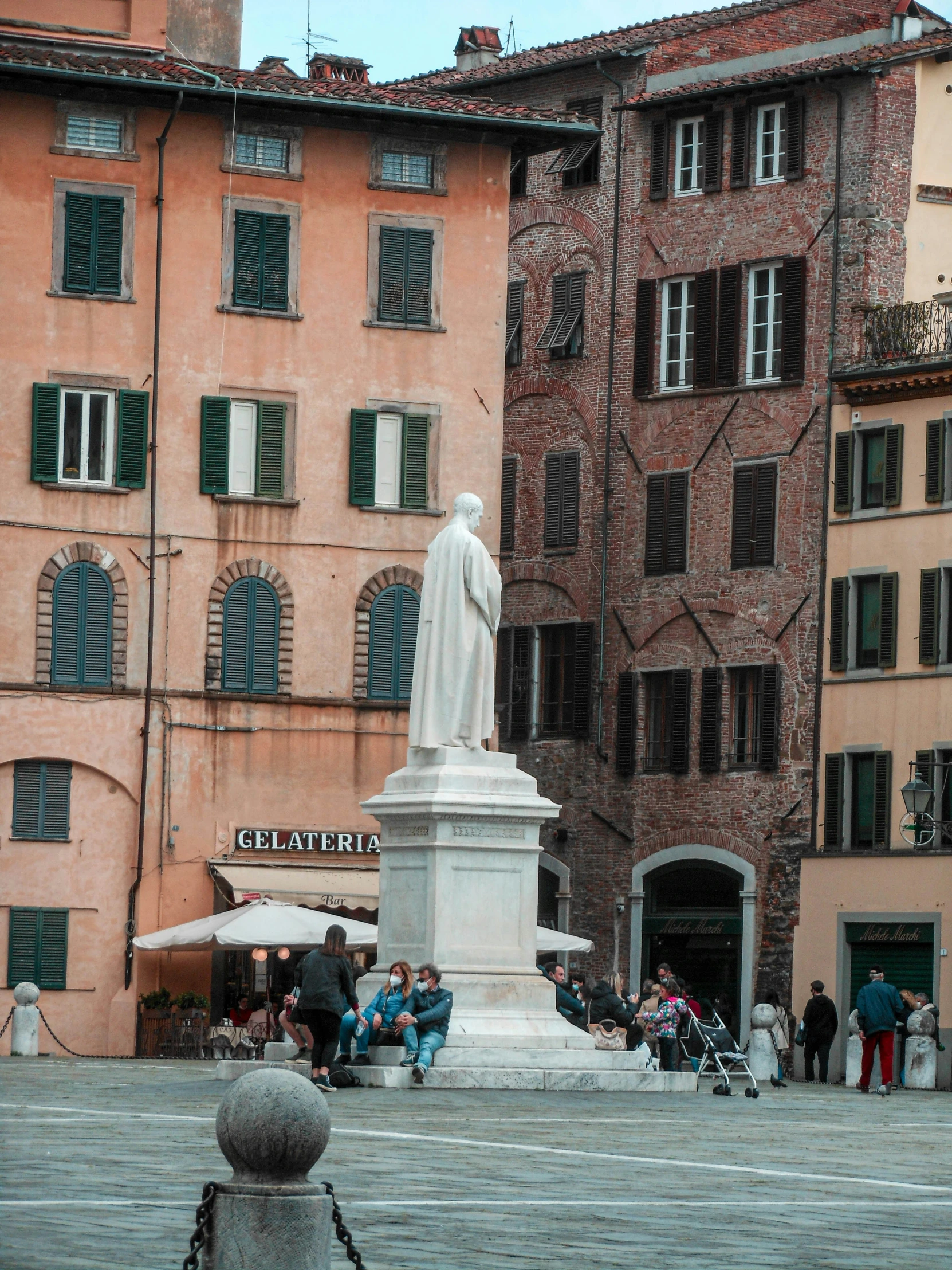 a group of people standing around a white statue in front of pink brick buildings