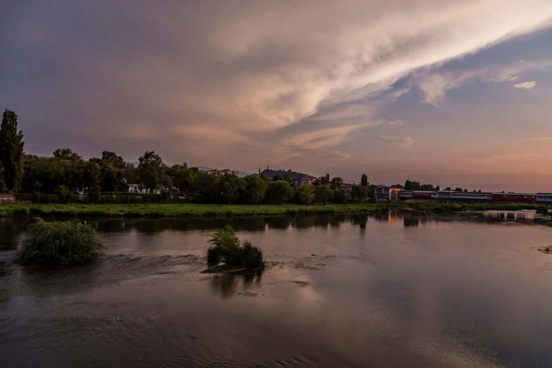 a lake at dusk with clouds above the water and boats in the distance