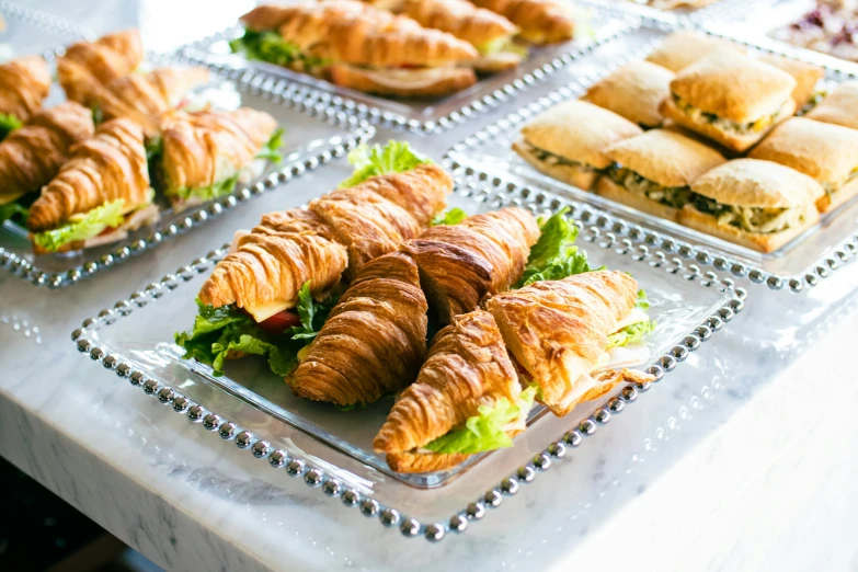 a buffet of sandwiches and croissants with lettuce and tomato