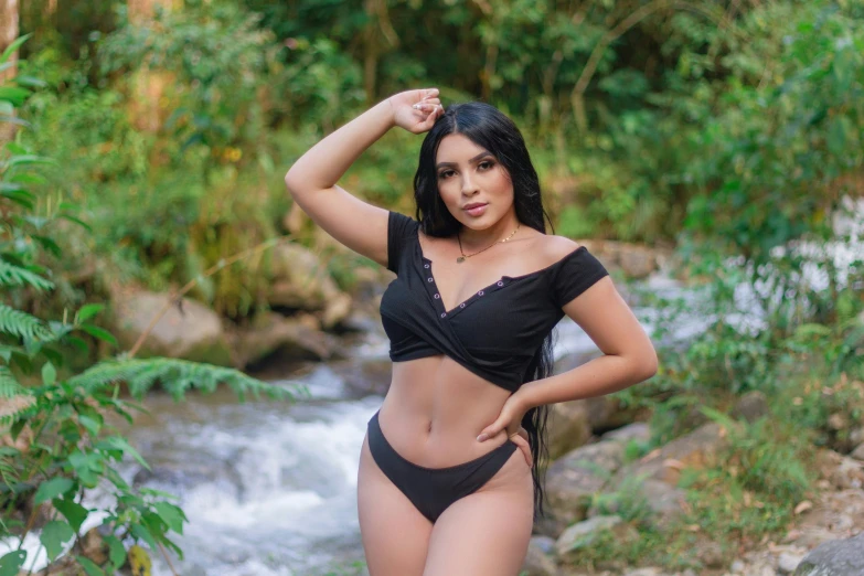 a woman in black swimsuit by stream posing for the camera